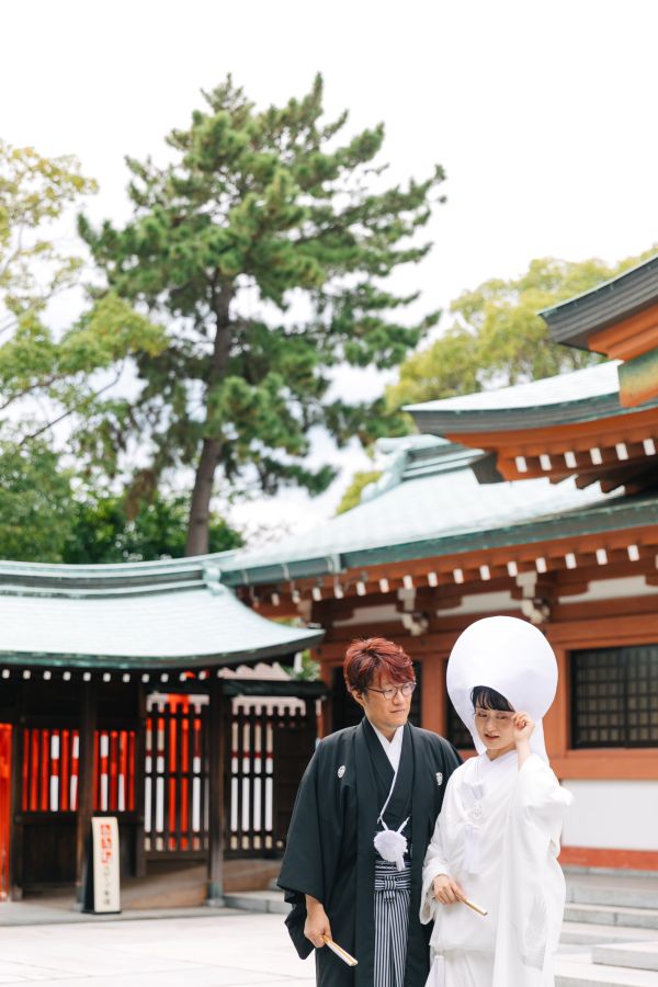 今治城内鎮座 吹揚神社で挙げられたお客様の結婚式写真　神社の前で写真を撮る紋付袴姿の新郎様と白無垢綿帽子をつけた新婦様　