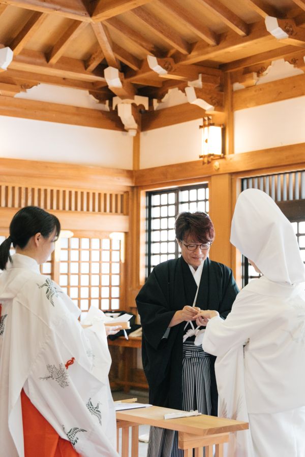 今治城内鎮座 吹揚神社で挙げられたお客様の結婚式写真　神前式で指輪の交換を行う紋付袴姿の新郎様と白無垢綿帽子をつけた新婦様