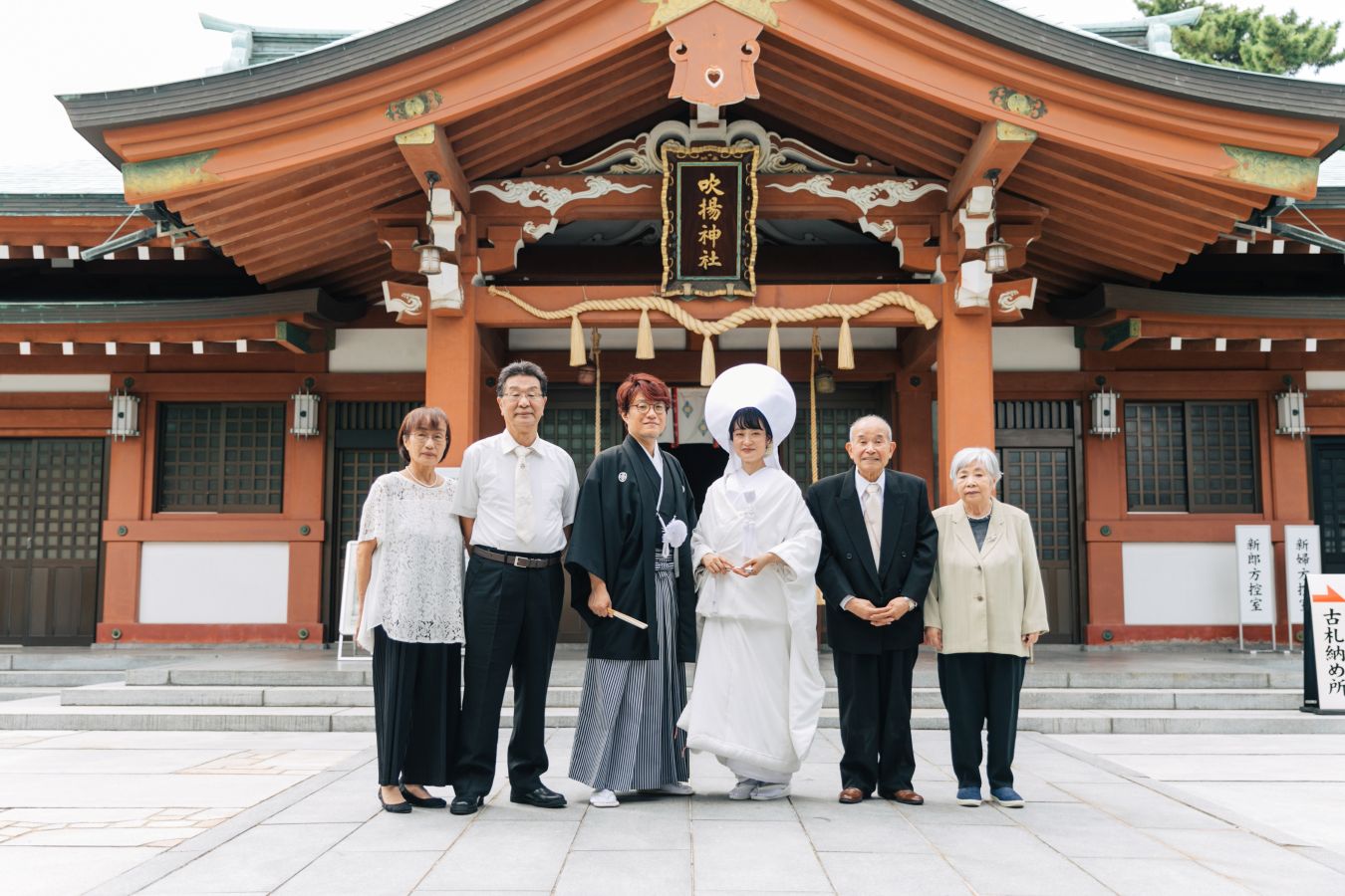 今治城内鎮座 吹揚神社で挙げられたお客様の結婚式写真　神社の前で家族写真を撮る紋付袴姿の新郎様と白無垢綿帽子をつけた新婦様