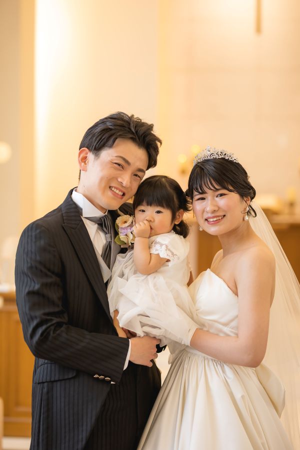 ANAクラウンプラザホテル松山でご結婚式を挙げられたお客様の写真　お子様を抱っこして寄り添うタキシードウェディングドレス姿の新郎新婦様