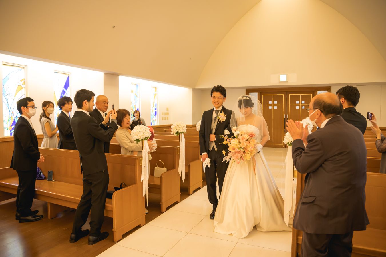 ANAクラウンプラザホテル松山でご結婚式を挙げられたお客様の写真　ご家族様の拍手と笑顔の中ご入場されるタキシードウェディングドレス姿の新郎新婦様