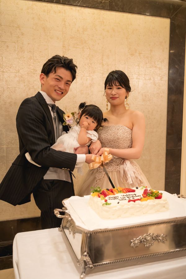 ANAクラウンプラザホテル松山でご結婚式を挙げられたお客様の写真　ウェディングケーキ入刀をするタキシードカラードレス姿の新郎新婦様とお子様