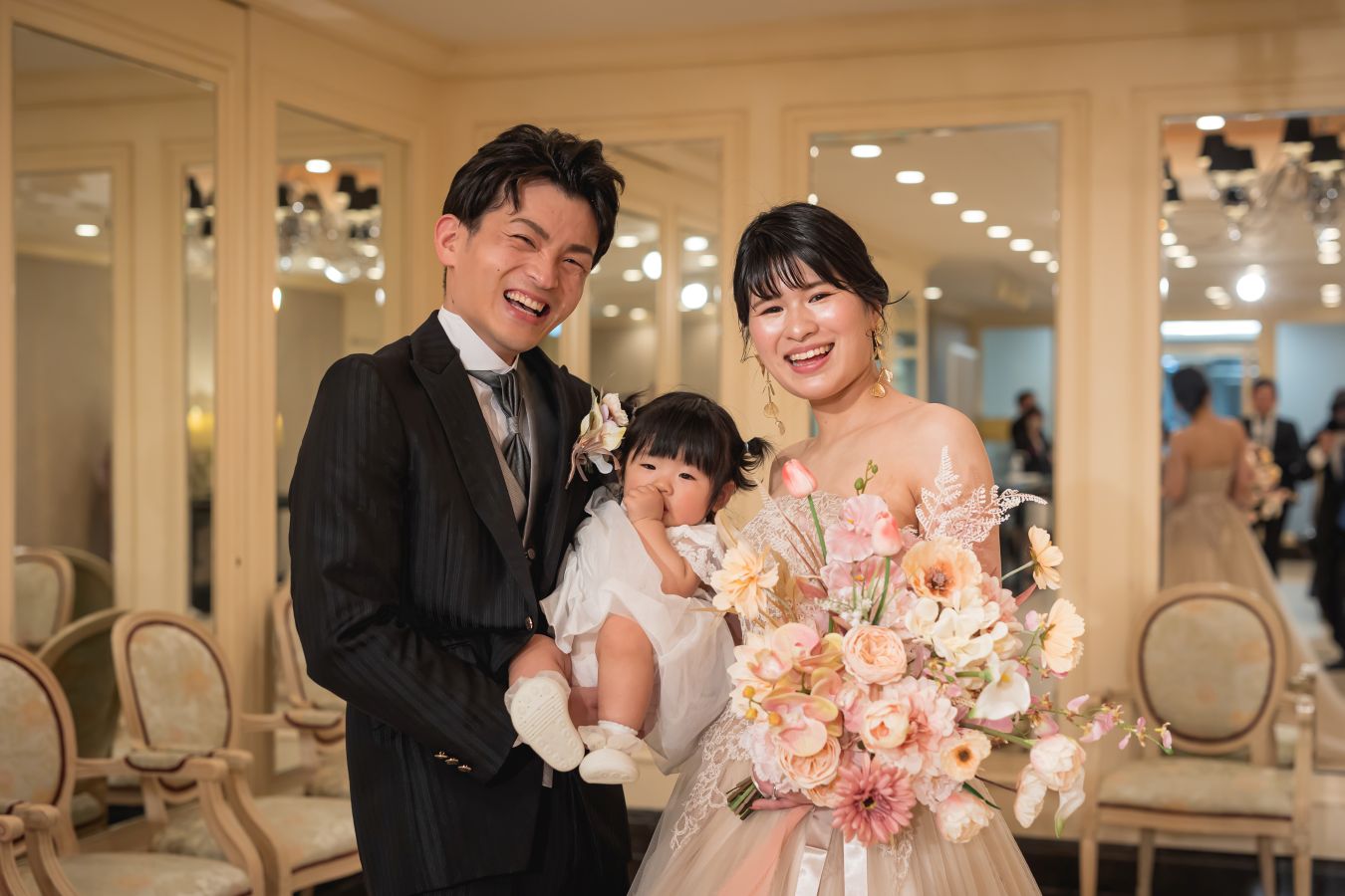 ANAクラウンプラザホテル松山でご結婚式を挙げられたお客様の写真　ご家族様をお見送り後ほっとした表情でお写真を撮るタキシードカラードレス姿の新郎新婦様とお子様