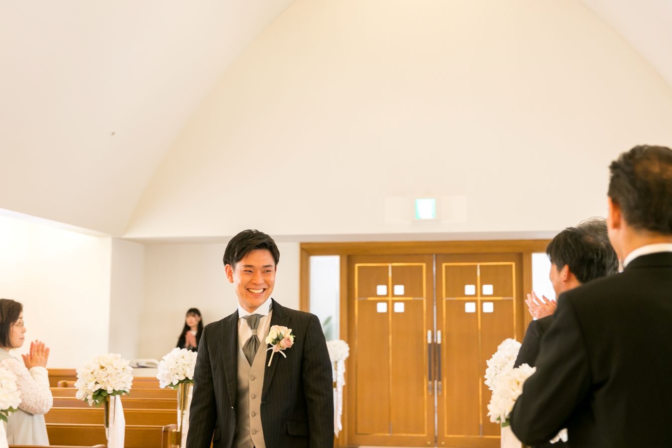ANAクラウンプラザホテル松山でご結婚式を挙げられたお客様の写真　ご家族様に笑顔を見せながらご入場されるタキシード姿の新郎様