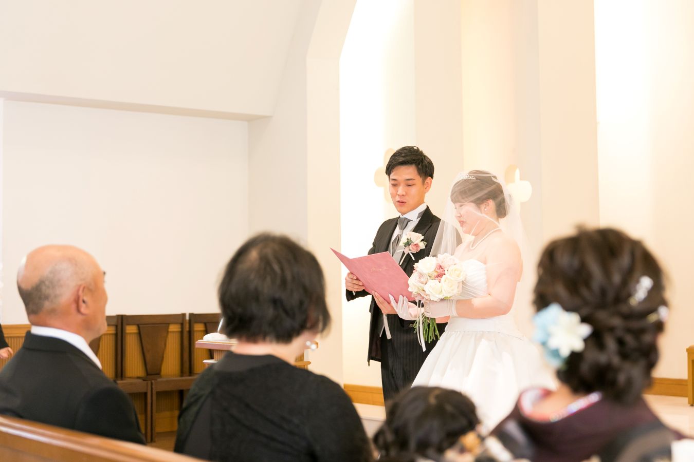 ANAクラウンプラザホテル松山でご結婚式を挙げられたお客様の写真　ご家族様の前で結婚の誓いを立てるタキシードウェディングドレス姿の新郎新婦様