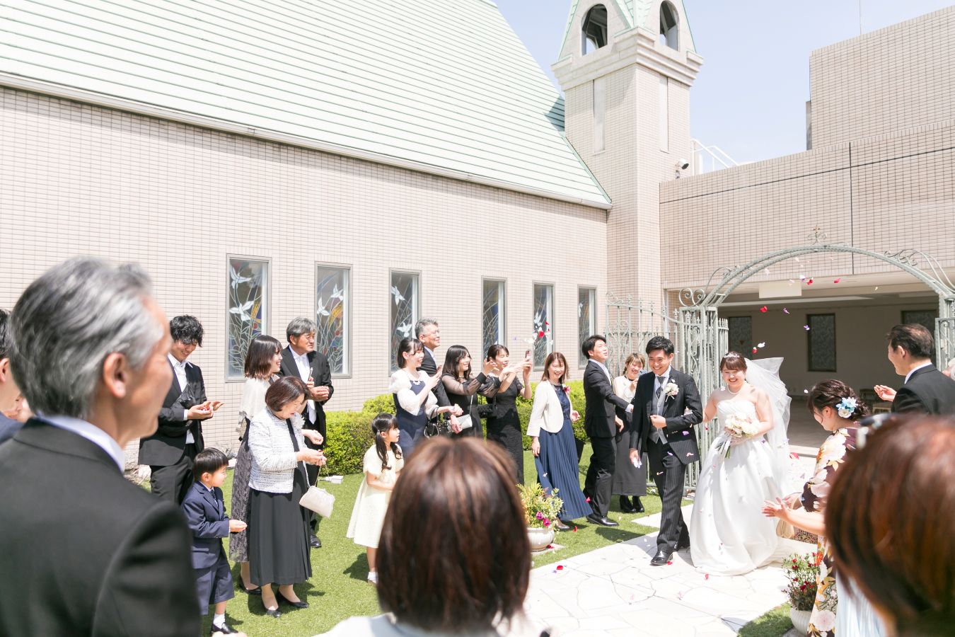 ANAクラウンプラザホテル松山でご結婚式を挙げられたお客様の写真　ガーデンでゲストの皆様から祝福のフラワーシャワーで迎えられたタキシードウェディングドレス姿の新郎新婦様