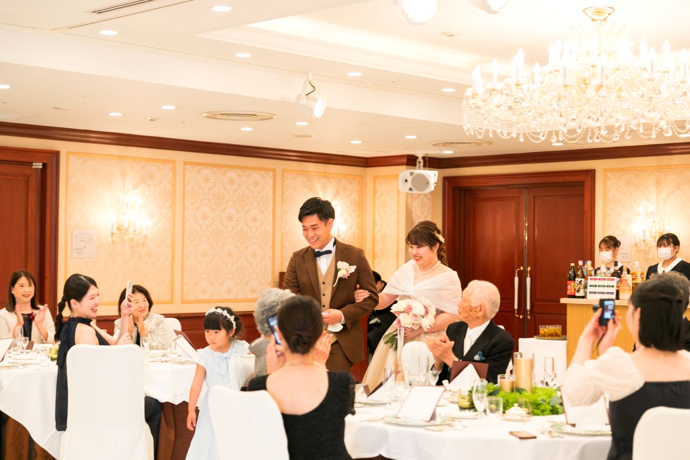 ANAクラウンプラザホテル松山でご結婚式を挙げられたお客様の写真　ゲストの皆様に迎えられ会食会場へ笑顔でご入場されるお色直しをしたタキシードカラードレス姿の新郎新婦様