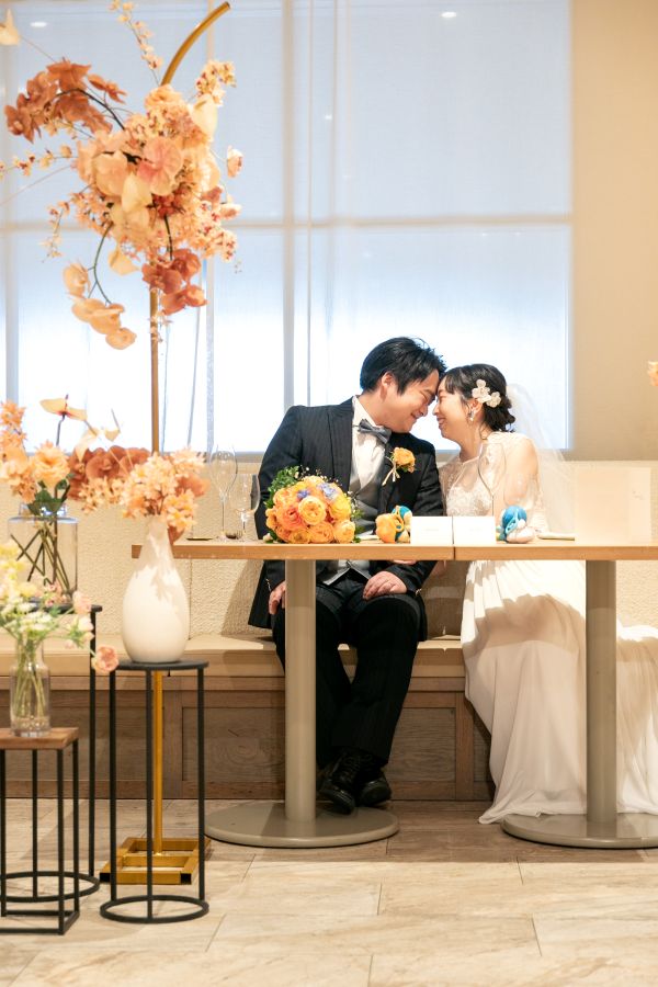 HOTEL LEPO CAHAL レストランAINOでご結婚式を挙げられたお客様の写真　レストランのメインテーブルに掛けて額を寄せ合うタキシードウェディングドレス姿の新郎新婦様