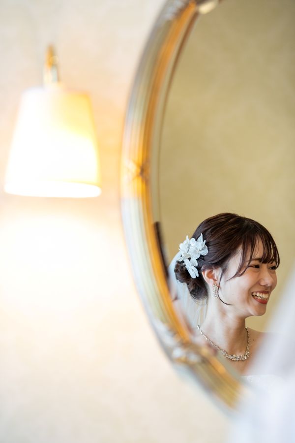 ANAクラウンプラザホテル松山でご結婚式を挙げられたお客様の写真　ブライズルームで鏡越しに新郎様へ微笑みかけるウェディングドレス姿の新婦様