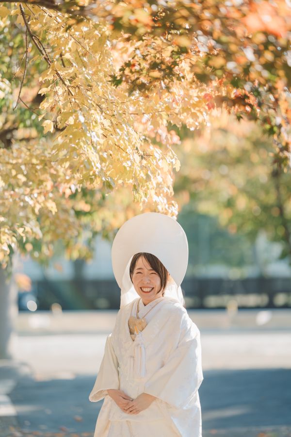 愛媛縣護國神社でご結婚式を挙げられたお客様の写真　色づいた木の下で笑顔を見せてくれた白無垢綿帽子姿の新婦様